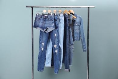 Photo of Rack with stylish jeans and denim clothes on color background