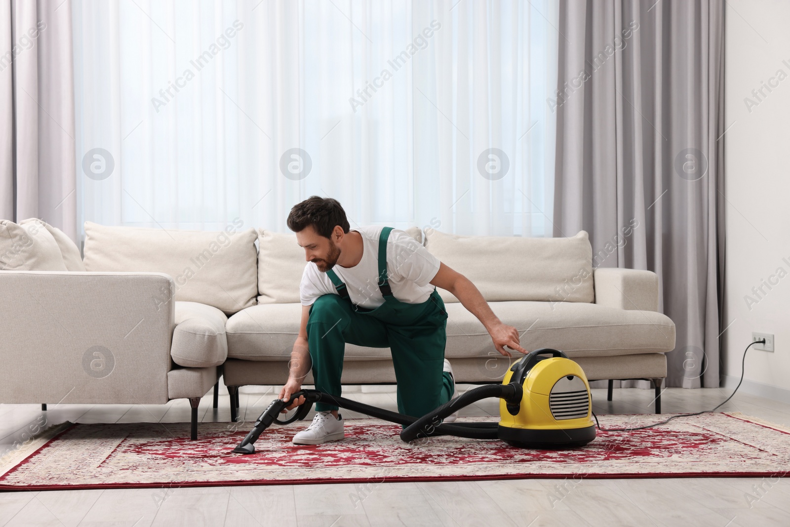 Photo of Dry cleaner's employee hoovering carpet with vacuum cleaner in room