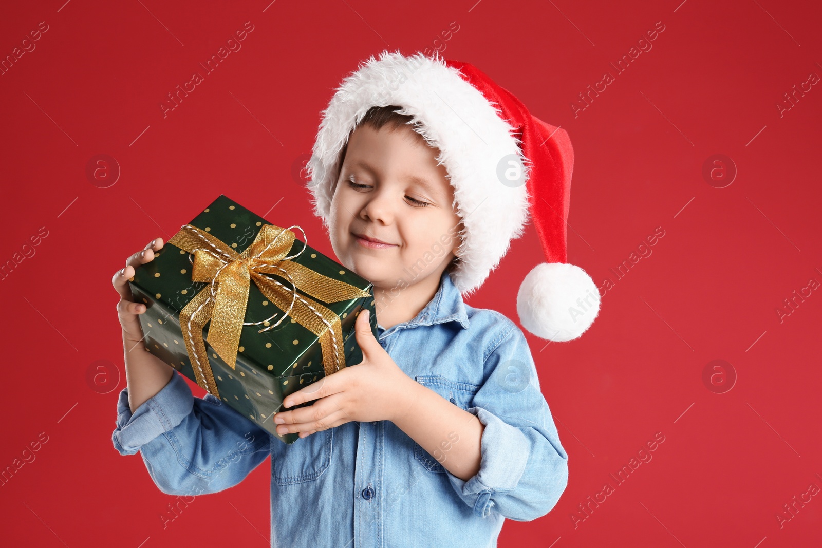 Photo of Cute child in Santa hat with Christmas gift on red background