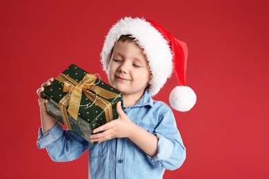 Photo of Cute child in Santa hat with Christmas gift on red background