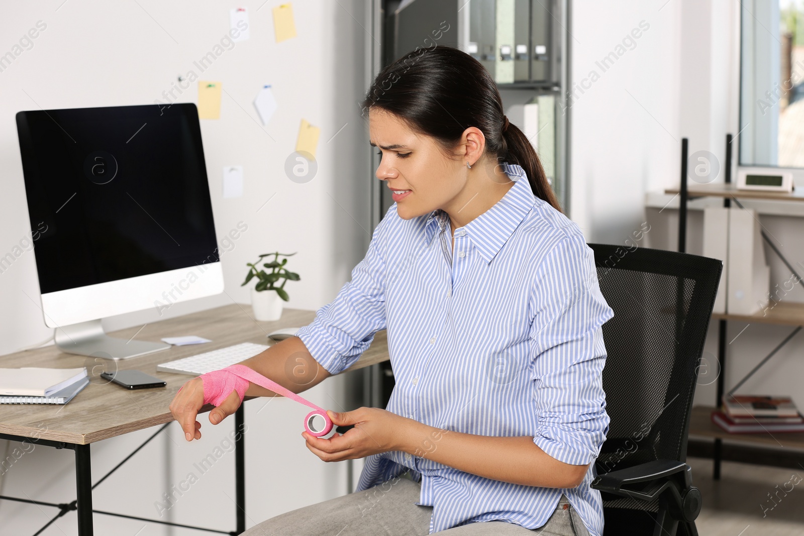 Photo of Young woman applying medical bandage onto hand in office