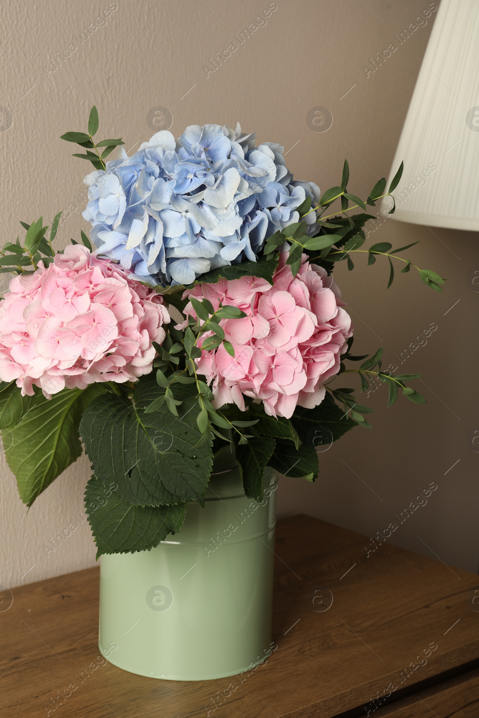 Photo of Beautiful hortensia flowers in can on wooden table against beige background