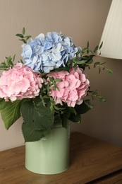 Beautiful hortensia flowers in can on wooden table against beige background