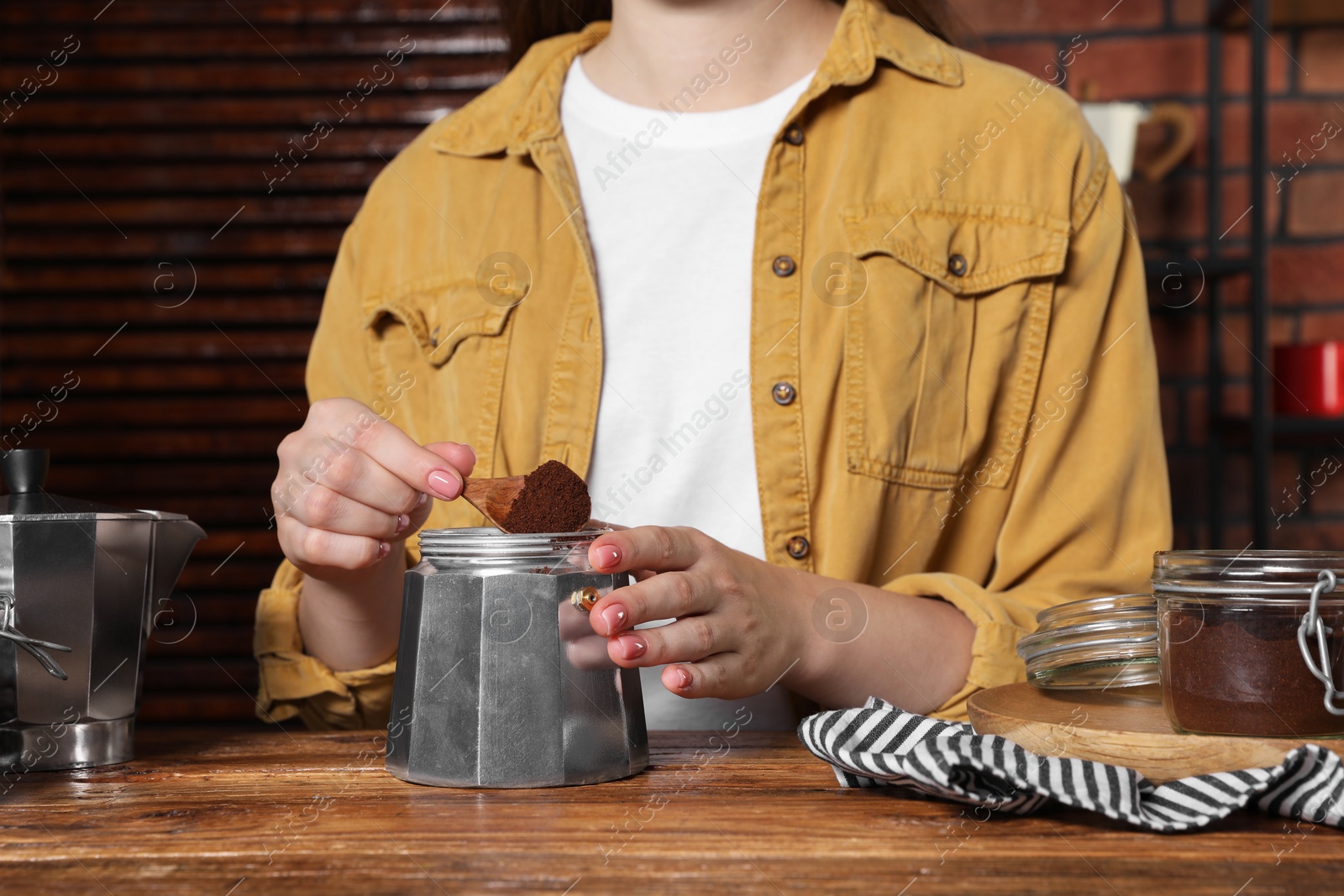 Photo of Woman putting ground coffee into moka pot at wooden table, closeup