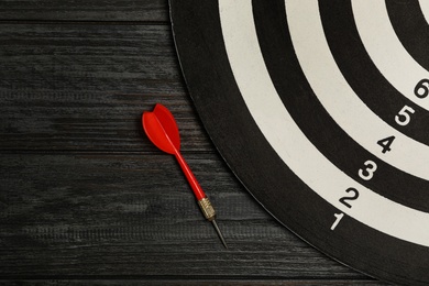 Dart board with color arrow on black wooden background, top view. Space for text