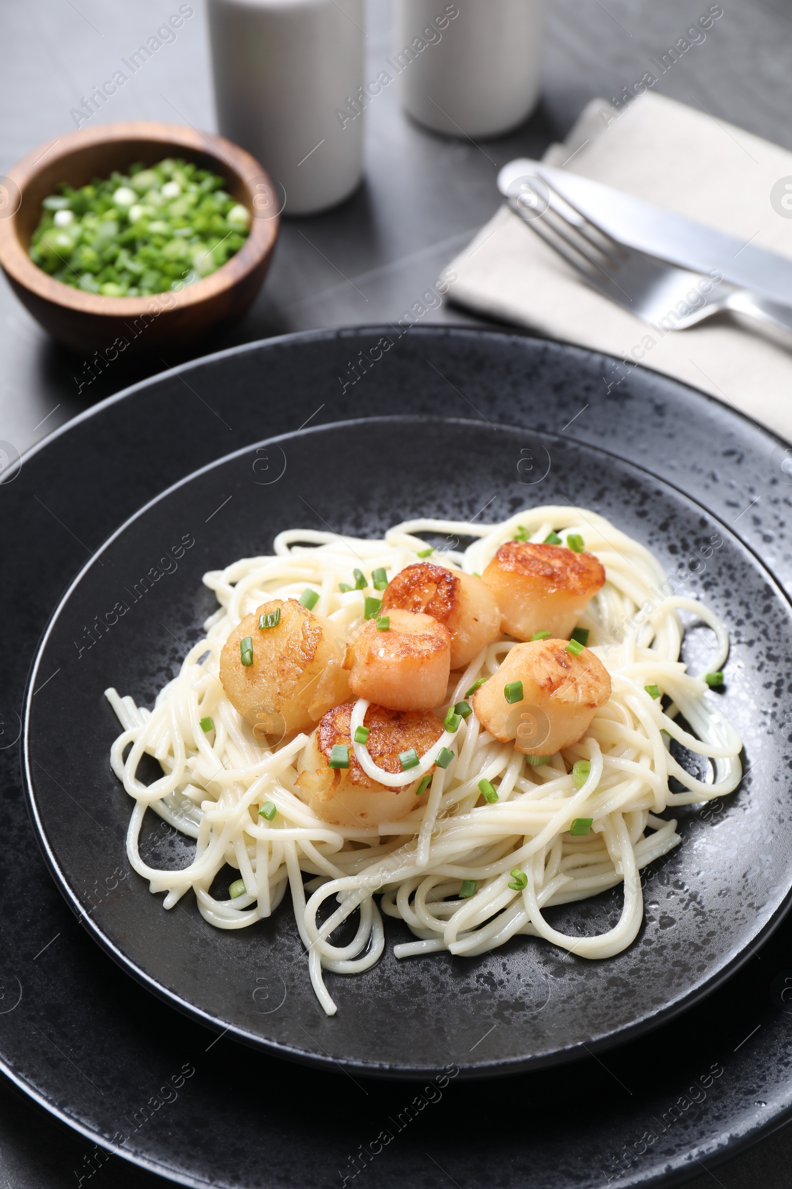 Photo of Delicious scallop pasta with green onion served on grey table