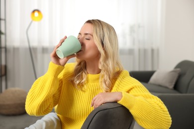 Beautiful woman in stylish warm sweater drinking tea at home