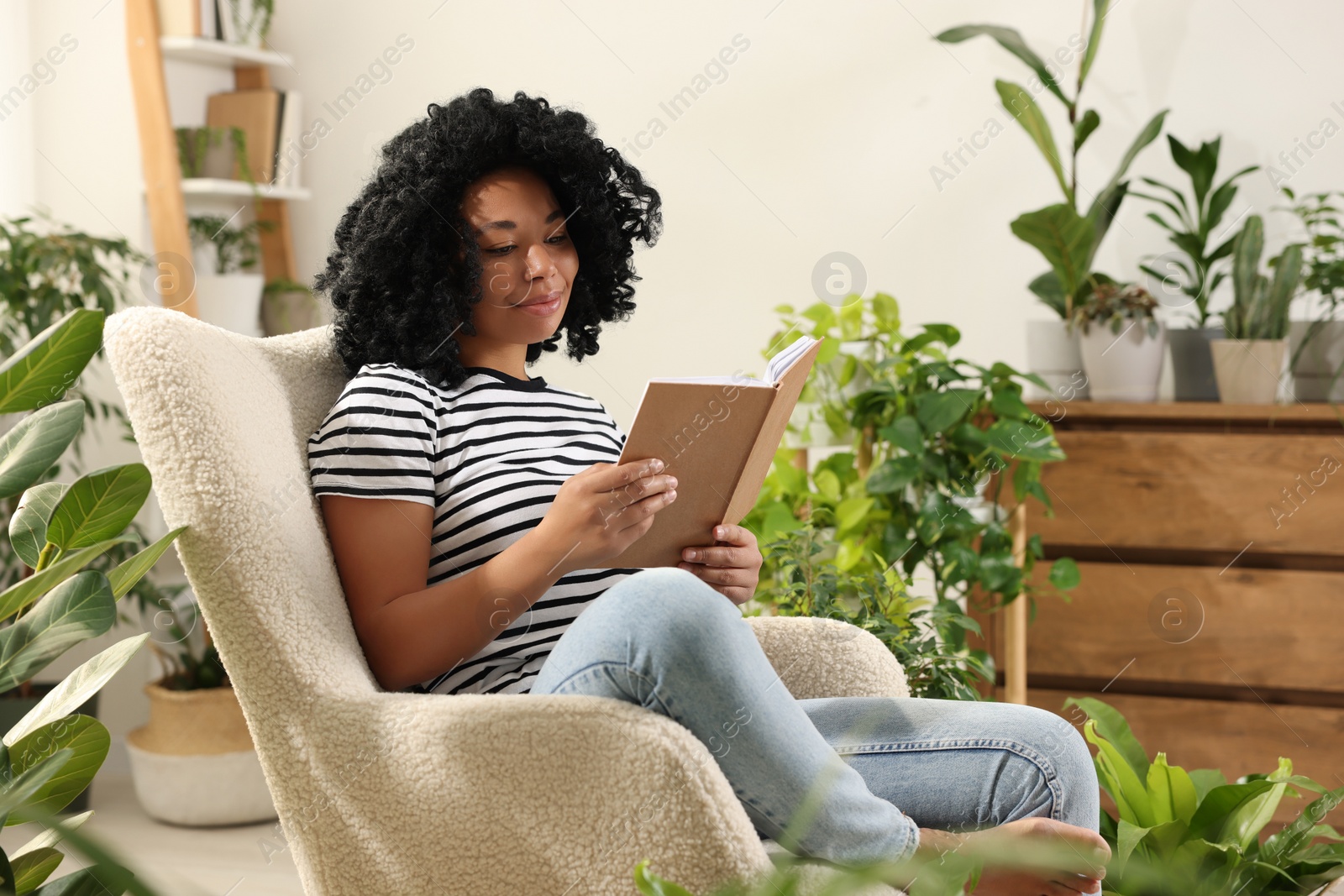 Photo of Relaxing atmosphere. Woman reading book near houseplants at home