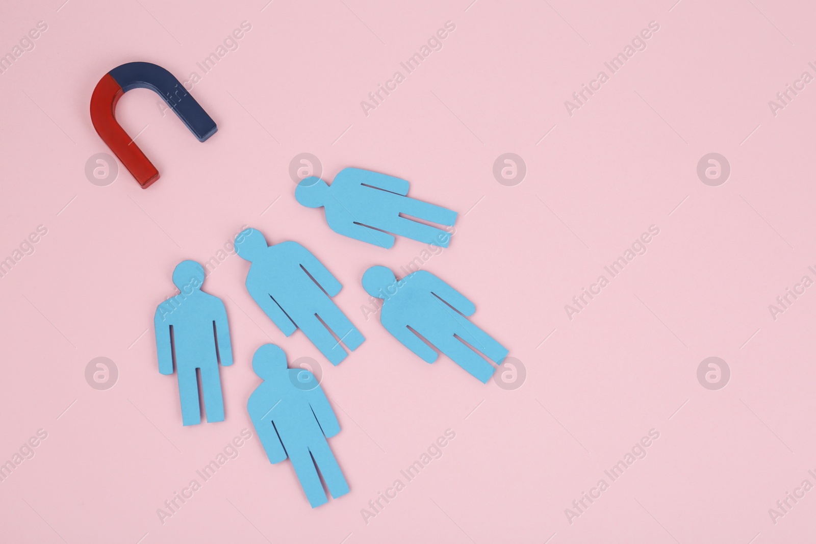 Photo of Magnet attracting paper people on pink background, above view. Space for text