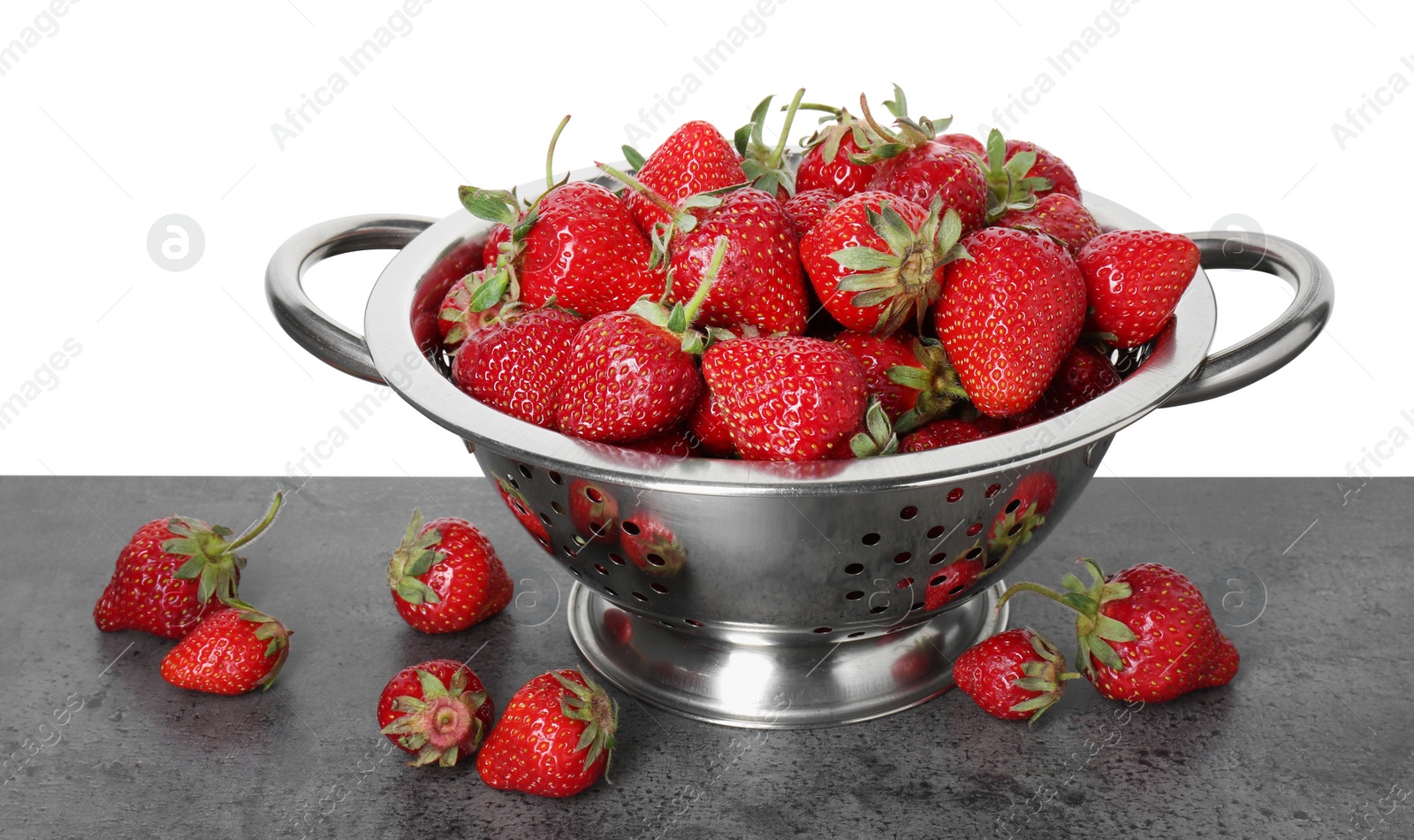 Photo of Metal colander with fresh strawberries on grey table against white background