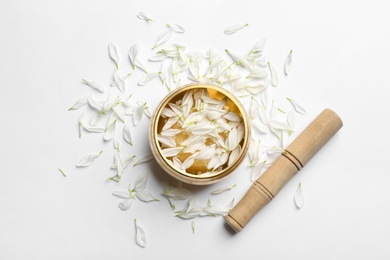 Photo of Golden singing bowl with petals and mallet on white background, flat lay. Sound healing