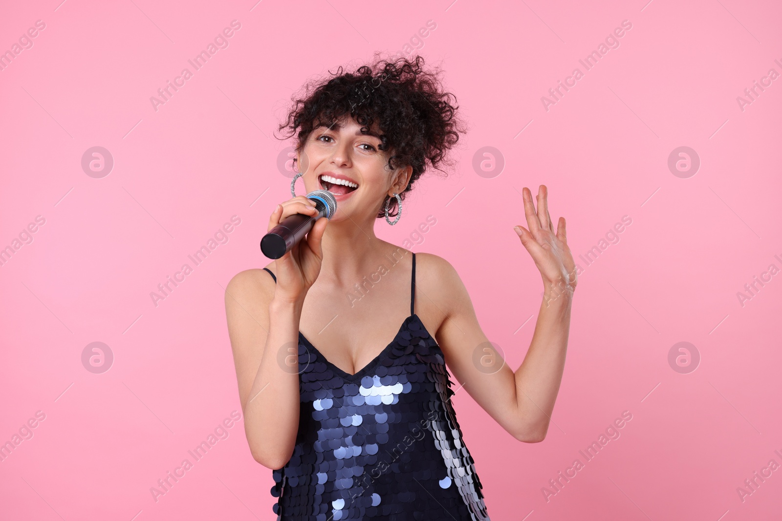 Photo of Beautiful young woman with microphone singing on pink background