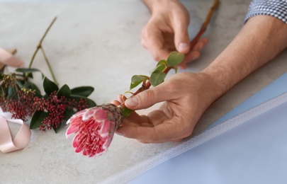 Male florist holding beautiful flower over table, closeup