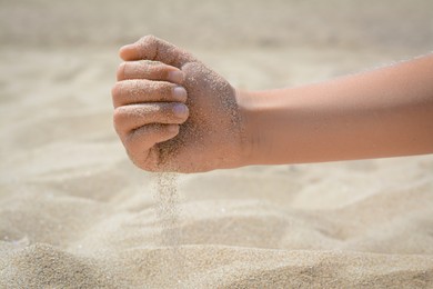 Photo of Child pouring sand from hand outdoors, closeup. Fleeting time concept