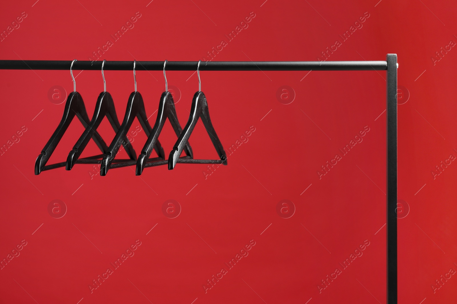 Photo of Black clothes hangers on rack against red background. Space for text