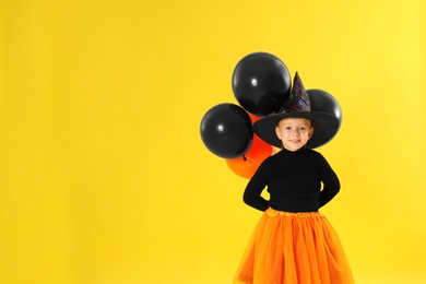 Photo of Cute little girl with balloons wearing Halloween costume on yellow background. Space for text