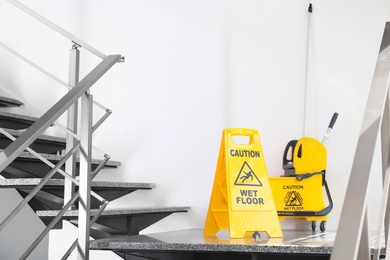 Photo of Safety sign with phrase Caution wet floor and mop bucket on stairs