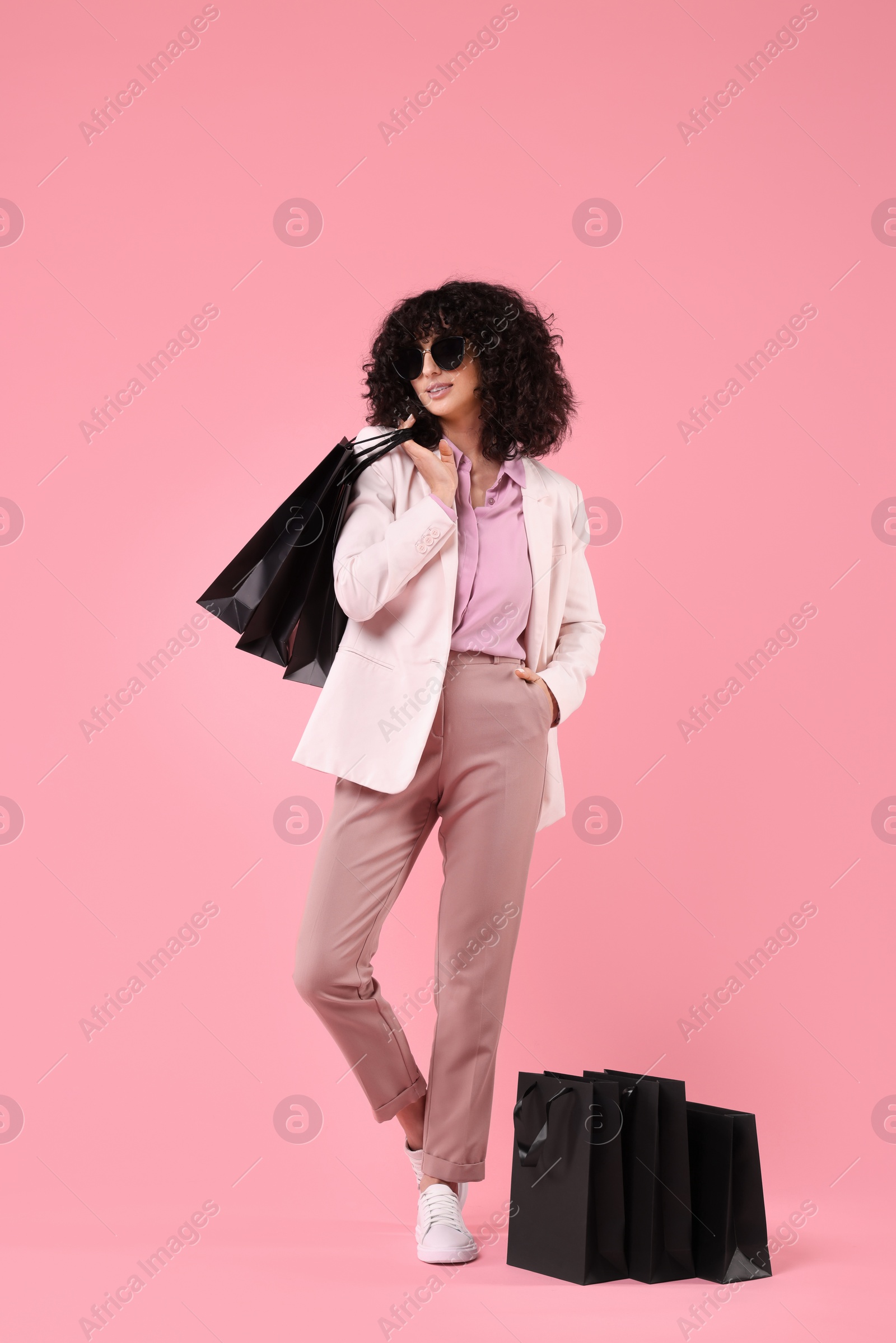 Photo of Happy young woman with shopping bags and stylish sunglasses on pink background