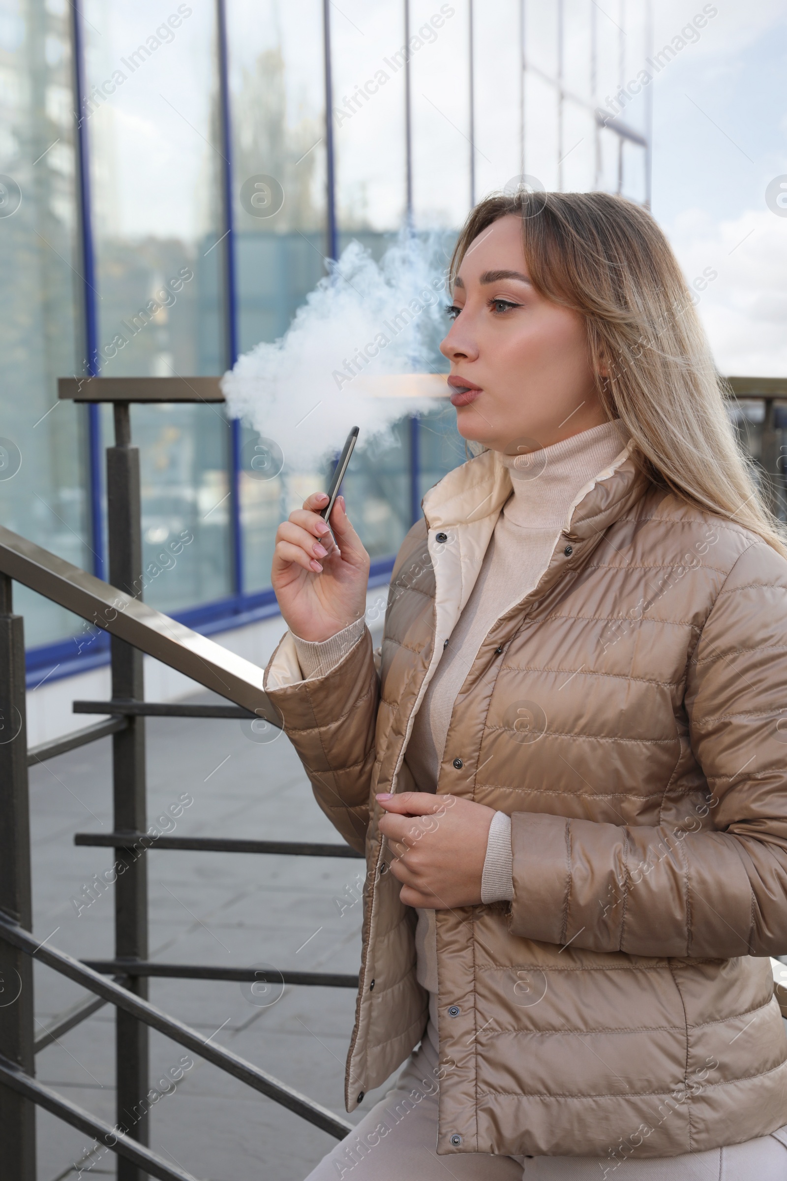 Photo of Beautiful young woman using disposable electronic cigarette outdoors