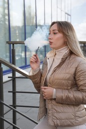 Photo of Beautiful young woman using disposable electronic cigarette outdoors