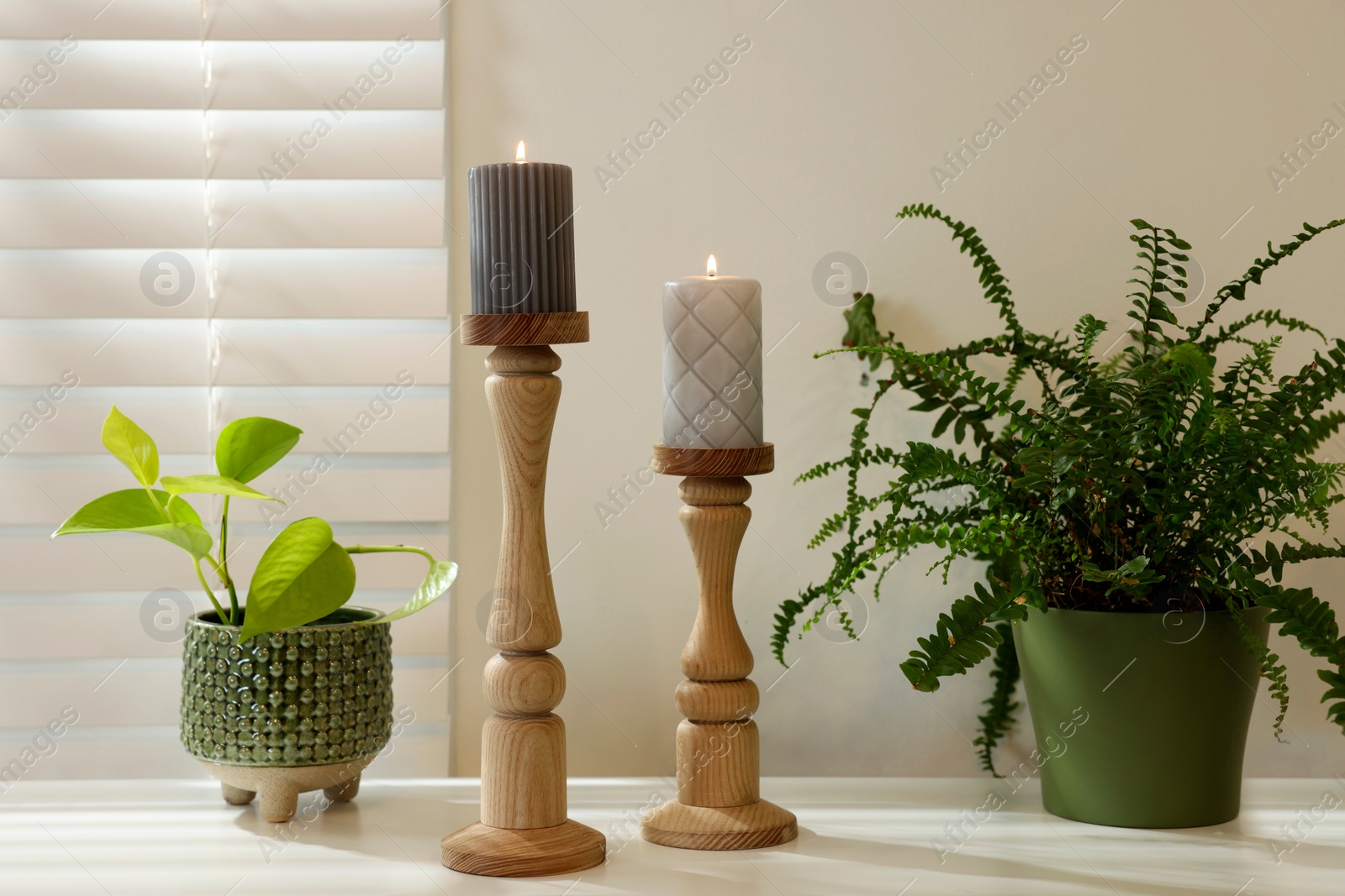 Photo of Pair of beautiful wooden candlesticks and houseplants on white table in room