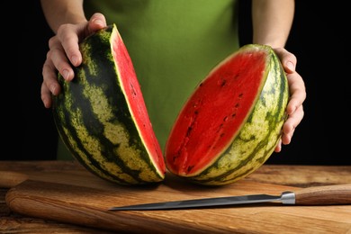 Photo of Woman with delicious halved watermelon at wooden table against black background, closeup