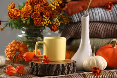 Beautiful autumn composition with cup of drink, pumpkins and flowers on wicker table