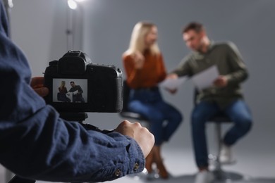 Casting call. Man and woman performing while camera operator filming them against grey background in studio, selective focus
