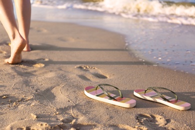 Photo of Closeup of woman and flip flops on sand near sea, space for text. Beach accessories