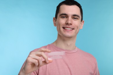 Young man with whitening strips on light blue background. Space for text