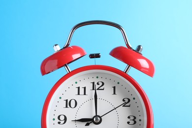 Photo of Red alarm clock on light blue background, closeup