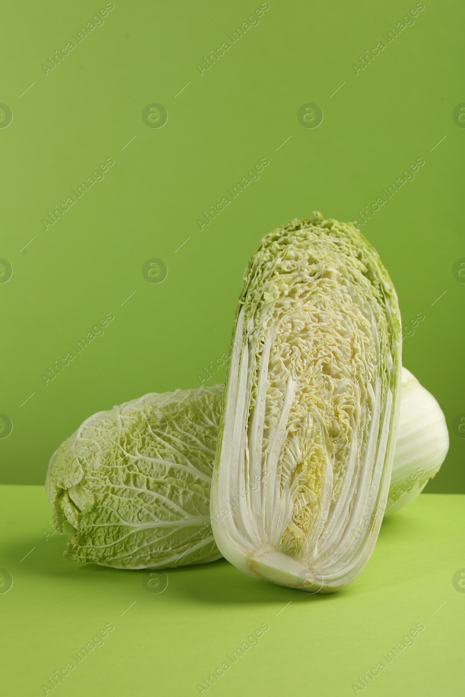 Photo of Whole and cut fresh Chinese cabbage on light green background