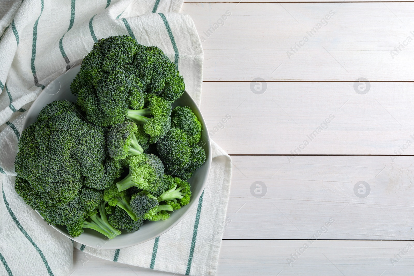 Photo of Bowl of fresh raw broccoli on white wooden table, top view. Space for text