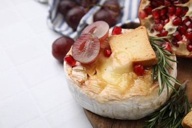 Photo of Tasty baked camembert with crouton, grape and rosemary on white tiled table, closeup. Space for text