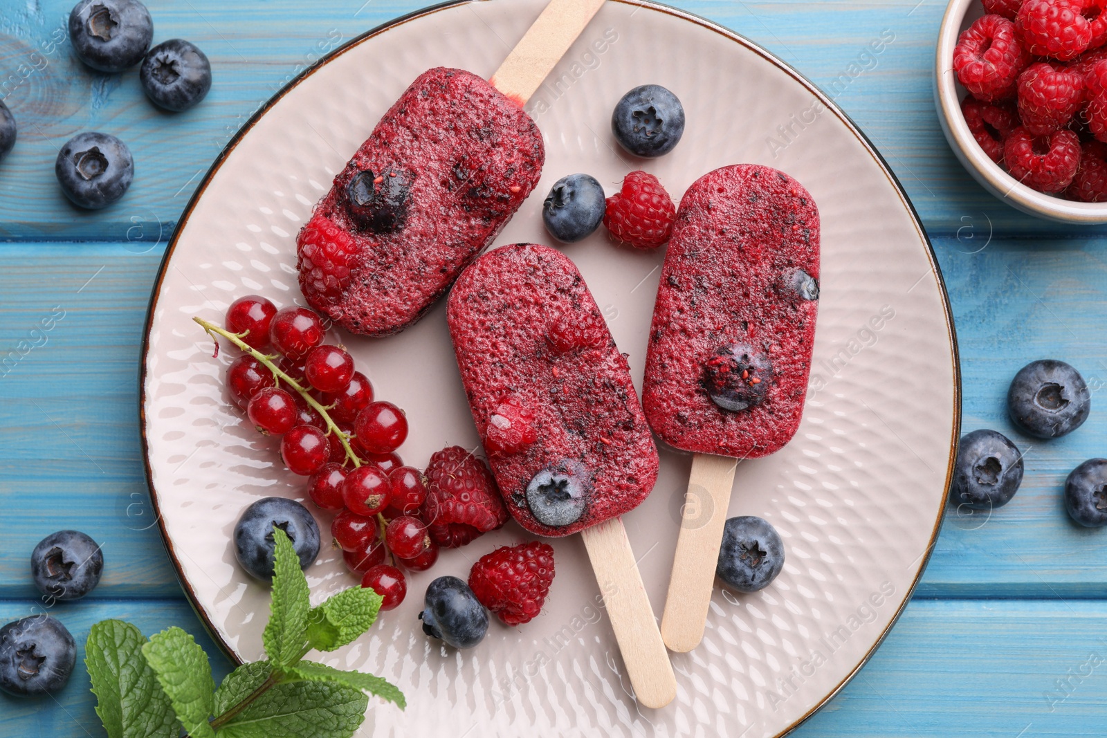 Photo of Plate of tasty berry ice pops on light blue wooden table, flat lay. Fruit popsicle