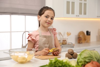 Photo of Little girl peeling potato at table in kitchen. Preparing vegetable