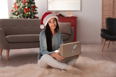 Photo of Beautiful young woman in Santa hat opening Christmas gift box at home