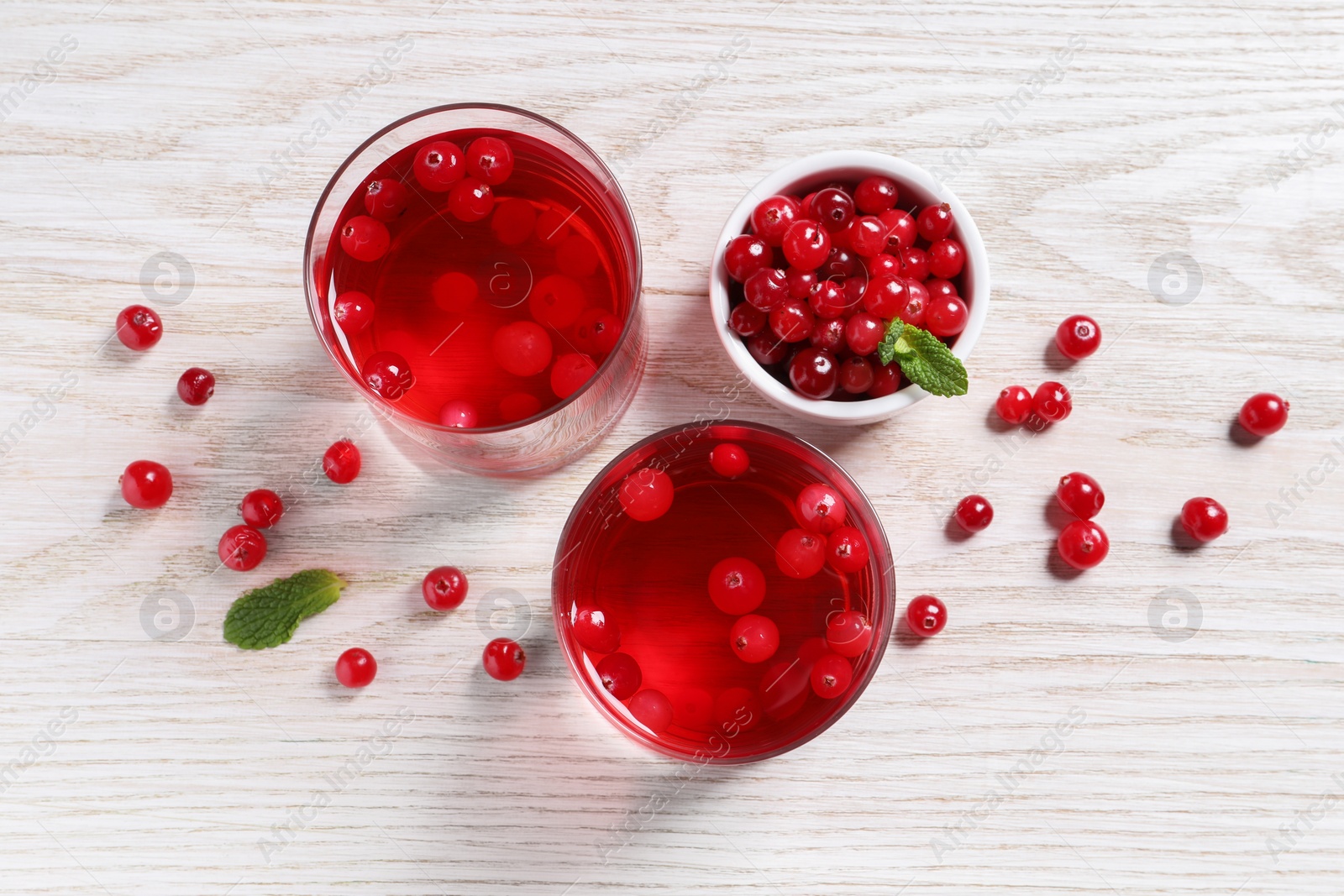 Photo of Tasty cranberry juice in glasses and fresh berries on white wooden table, flat lay