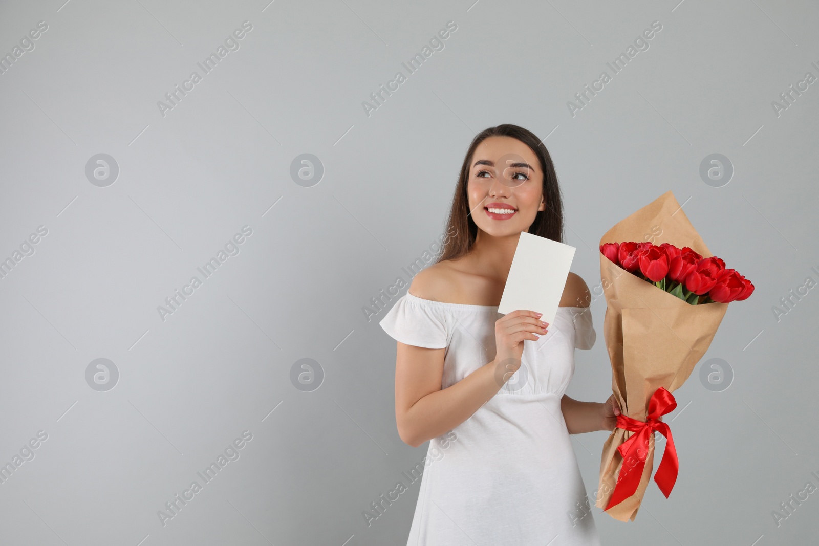 Photo of Happy woman with red tulip bouquet and greeting card on light grey background, space for text. 8th of March celebration