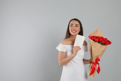 Happy woman with red tulip bouquet and greeting card on light grey background, space for text. 8th of March celebration