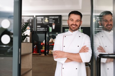 Photo of Happy baker in uniform at door of his cafe. Space for text