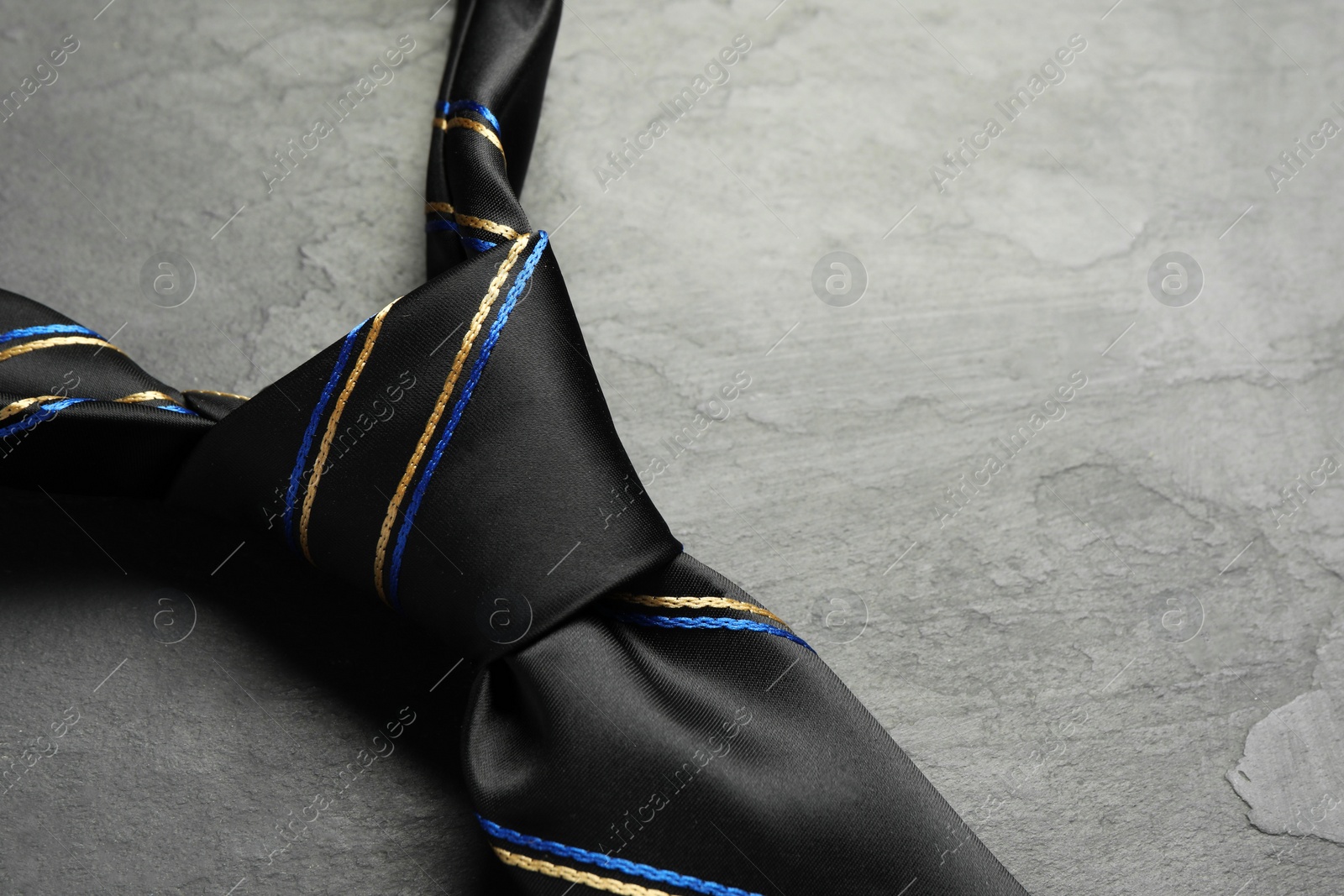 Photo of One striped necktie on grey textured table, closeup. Space for text