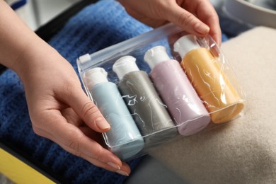 Woman with plastic bag of cosmetic travel kit packing suitcase, closeup