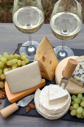 Photo of Different types of delicious cheeses, snacks and wine on wooden table outdoors