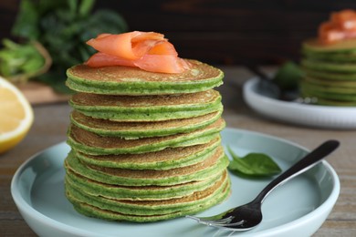 Tasty spinach pancakes with salmon on wooden table, closeup