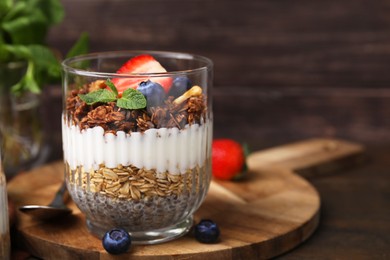 Photo of Tasty granola with berries, yogurt and chia seeds in glass on wooden table, space for text