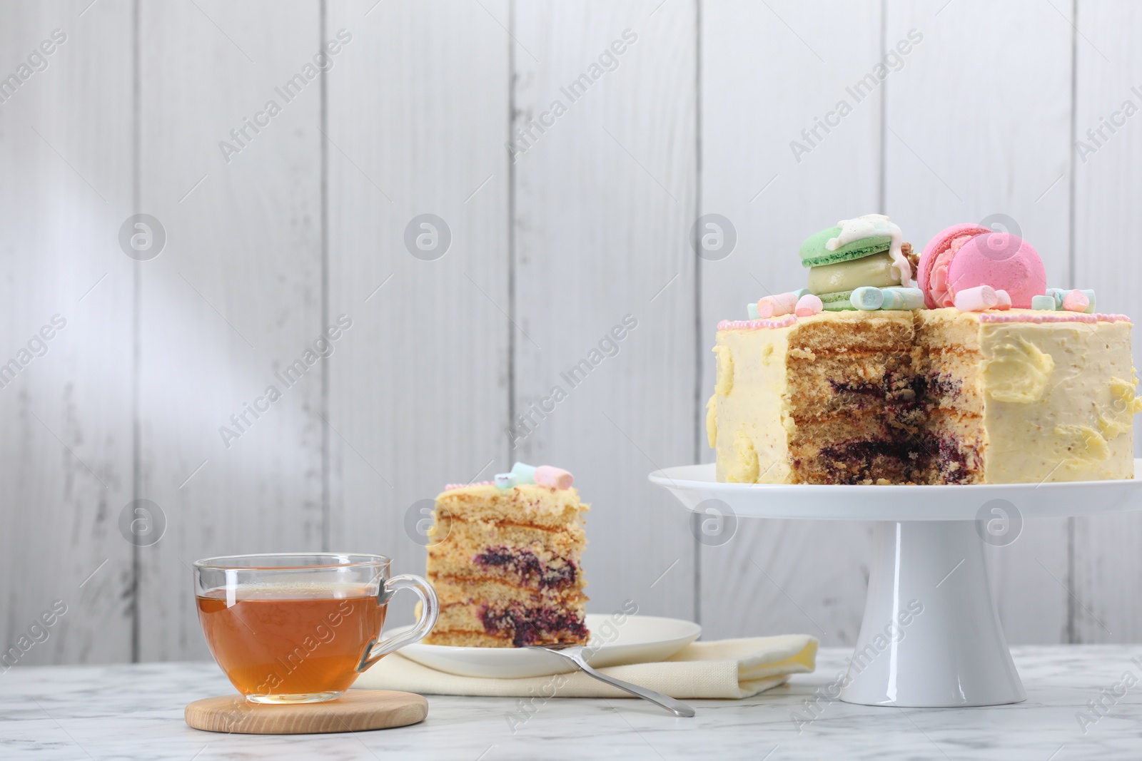 Photo of Delicious cake decorated with macarons and marshmallows and tea served on white marble table, space for text