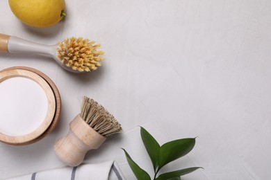 Photo of Cleaning brushes, baking soda, lemon and green leaves on white table, flat lay. Space for text