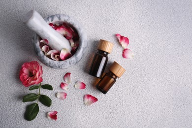 Photo of Glass bottles of aromatic essential oil, mortar with roses on white table, flat lay. Space for text