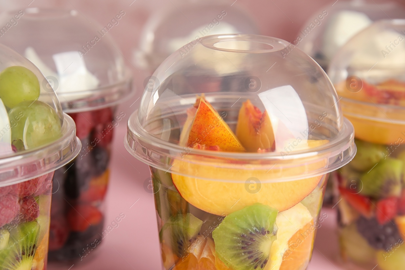 Photo of Fresh tasty fruit salad in plastic cups on pink table, closeup